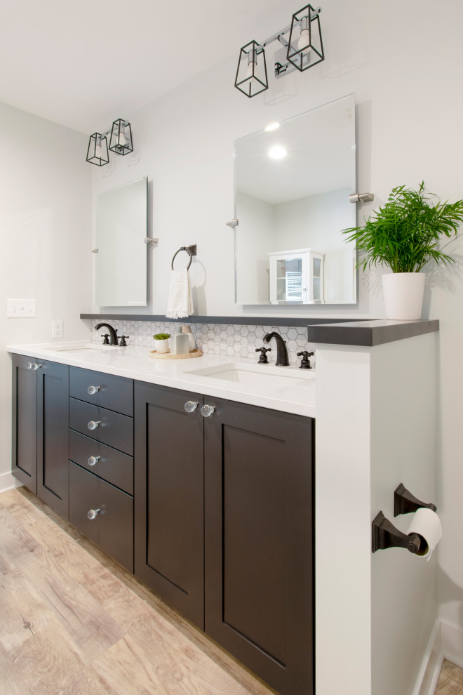 Photo of a medium sized contemporary ensuite bathroom in Milwaukee with shaker cabinets, black cabinets, a corner shower, a two-piece toilet, white tiles, metro tiles, grey walls, vinyl flooring, a submerged sink, engineered stone worktops, brown floors, a hinged door, white worktops, a wall niche, double sinks and a built in vanity unit.