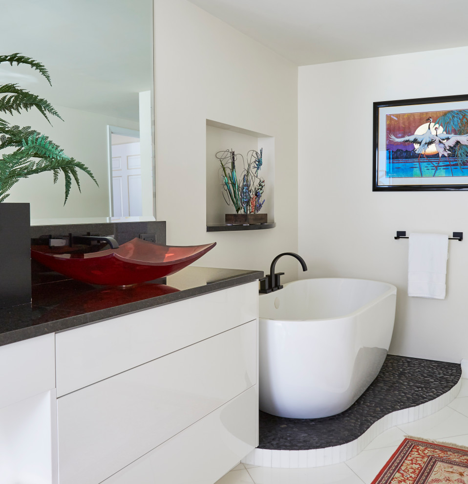 Photo of a medium sized contemporary ensuite bathroom with flat-panel cabinets, white cabinets, a freestanding bath, a double shower, white tiles, marble tiles, a vessel sink, granite worktops, a hinged door, black worktops, double sinks and a built in vanity unit.