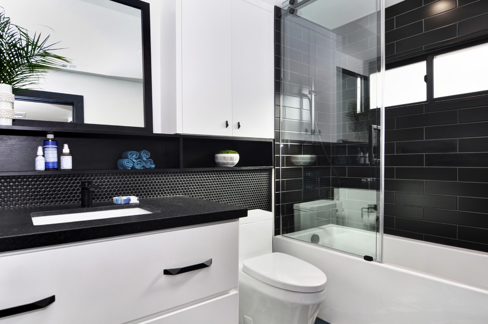 Exemple d'une salle de bain chic de taille moyenne pour enfant avec un placard à porte plane, des portes de placard blanches, une baignoire en alcôve, un combiné douche/baignoire, WC à poser, un carrelage noir, des carreaux de béton, un mur blanc, sol en béton ciré, un lavabo encastré, un plan de toilette en granite, un sol bleu, une cabine de douche à porte coulissante et un plan de toilette noir.