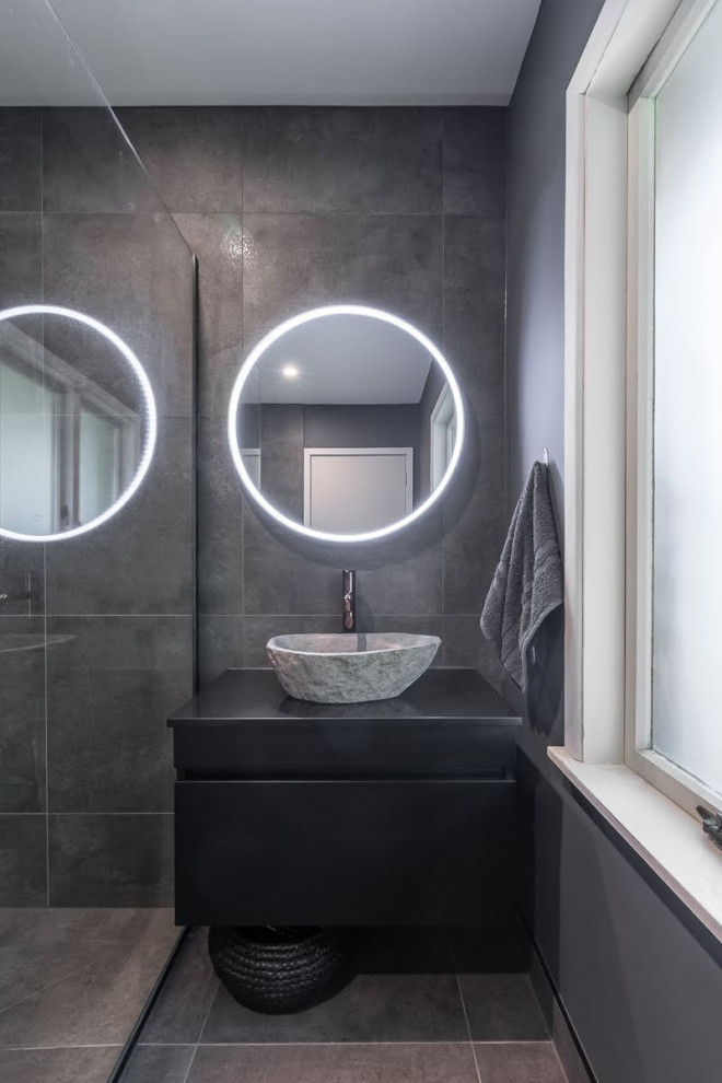 Foto di una stanza da bagno moderna di medie dimensioni con ante nere, piastrelle grigie, lavabo a bacinella, pavimento grigio e porta doccia a battente