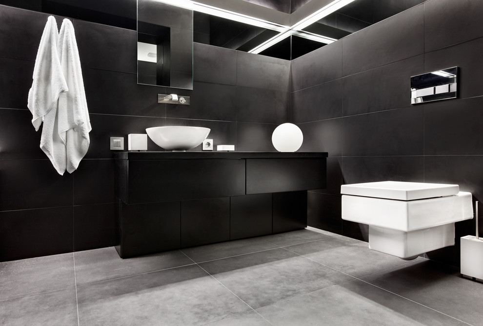 На фото: главная ванная комната среднего размера в современном стиле с плоскими фасадами, черными фасадами, черной плиткой, керамической плиткой, черными стенами, настольной раковиной, столешницей из дерева, биде и полом из цементной плитки