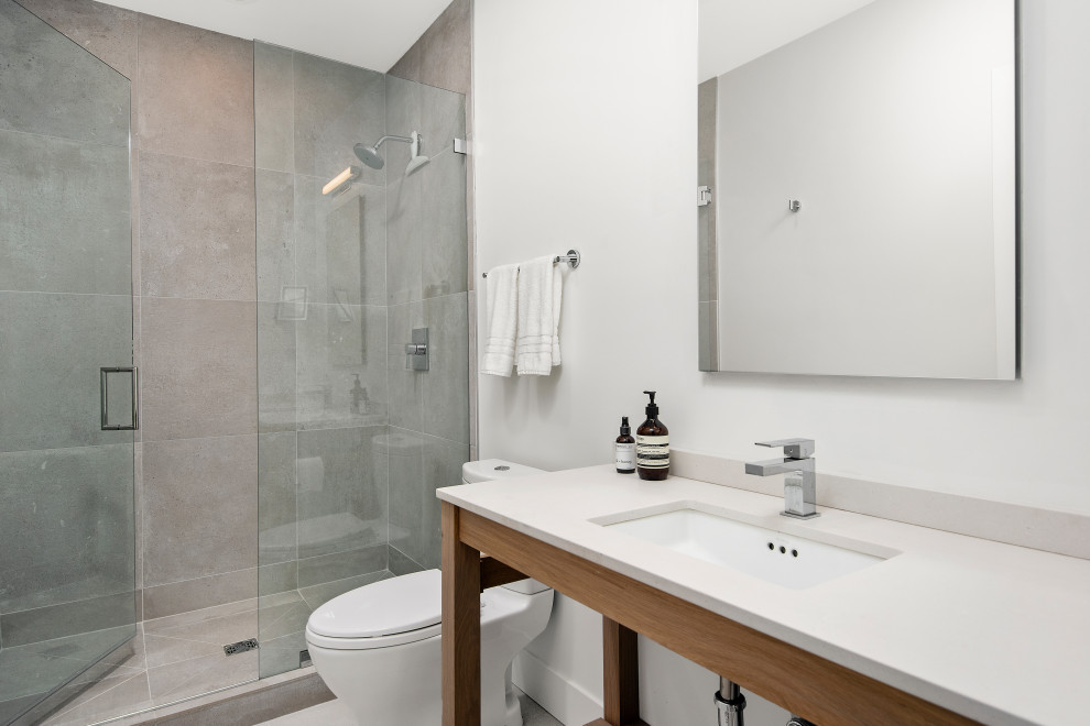 Inredning av ett modernt vit vitt badrum, med öppna hyllor, grå skåp, en öppen dusch, en toalettstol med hel cisternkåpa, grå kakel, porslinskakel, vita väggar, grått golv och dusch med gångjärnsdörr