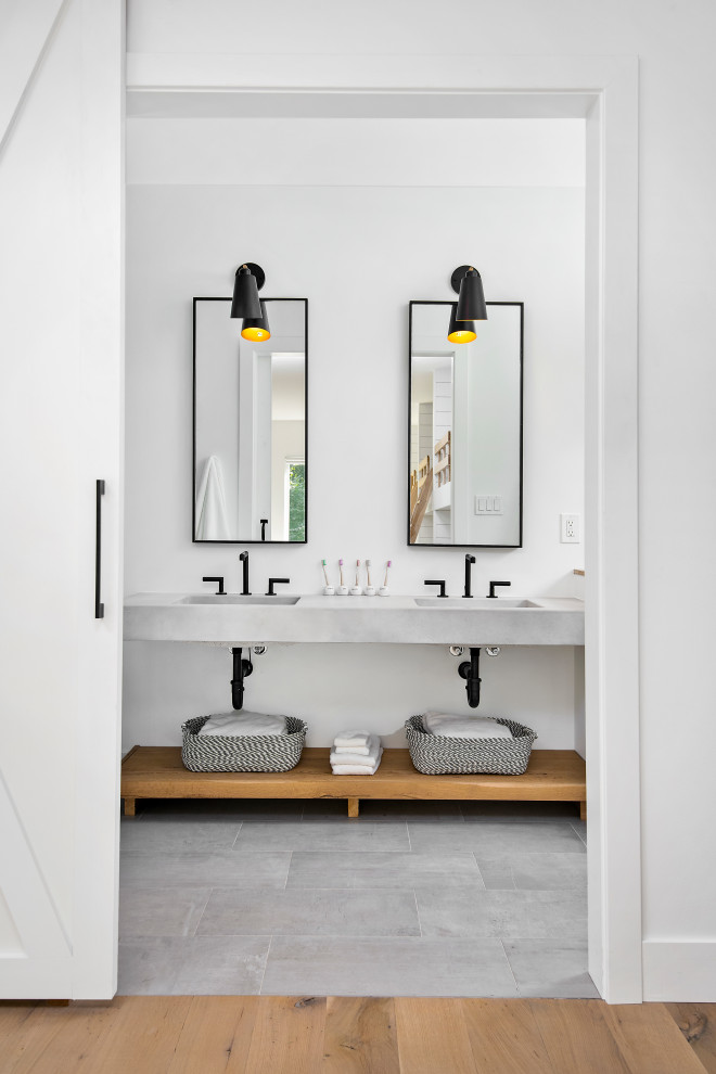 Modern bathroom with open cabinets, grey cabinets, a walk-in shower, a one-piece toilet, grey tiles, porcelain tiles, white walls, concrete worktops, grey floors, a hinged door and grey worktops.