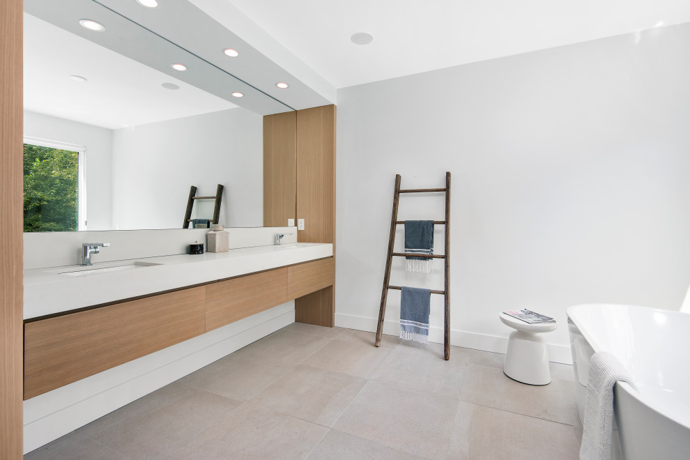 На фото: большая главная ванная комната в современном стиле с светлыми деревянными фасадами, отдельно стоящей ванной, душем без бортиков, унитазом-моноблоком, белыми стенами, бежевым полом, белой столешницей, врезной раковиной и плоскими фасадами