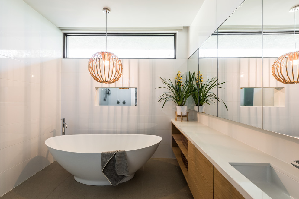 Modernes Badezimmer mit flächenbündigen Schrankfronten, hellbraunen Holzschränken, freistehender Badewanne, Unterbauwaschbecken, grauem Boden und weißer Waschtischplatte in Melbourne