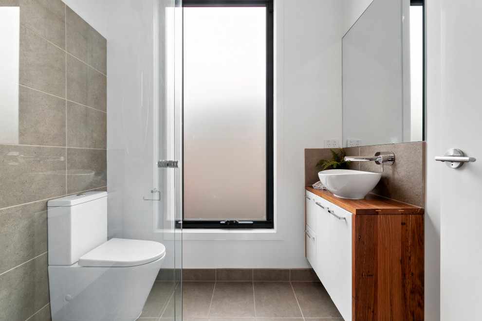Idéer för ett modernt brun badrum, med släta luckor, vita skåp, grå kakel, vita väggar, ett fristående handfat, träbänkskiva och grått golv