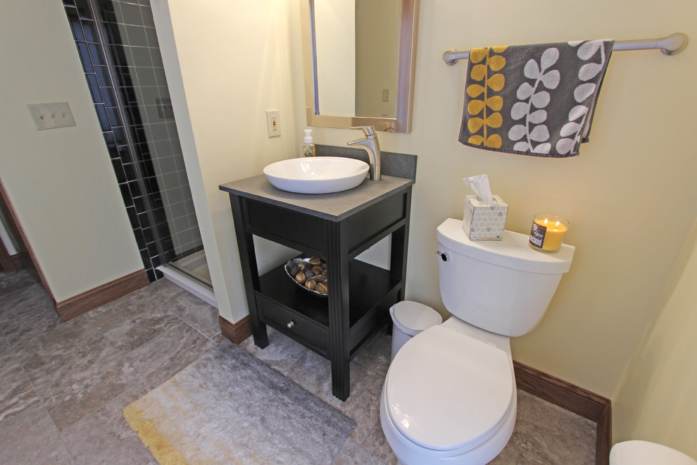 Klassisk inredning av ett mellanstort badrum, med ett fristående handfat, öppna hyllor, svarta skåp, en hörndusch, svart kakel, keramikplattor, gula väggar och klinkergolv i porslin