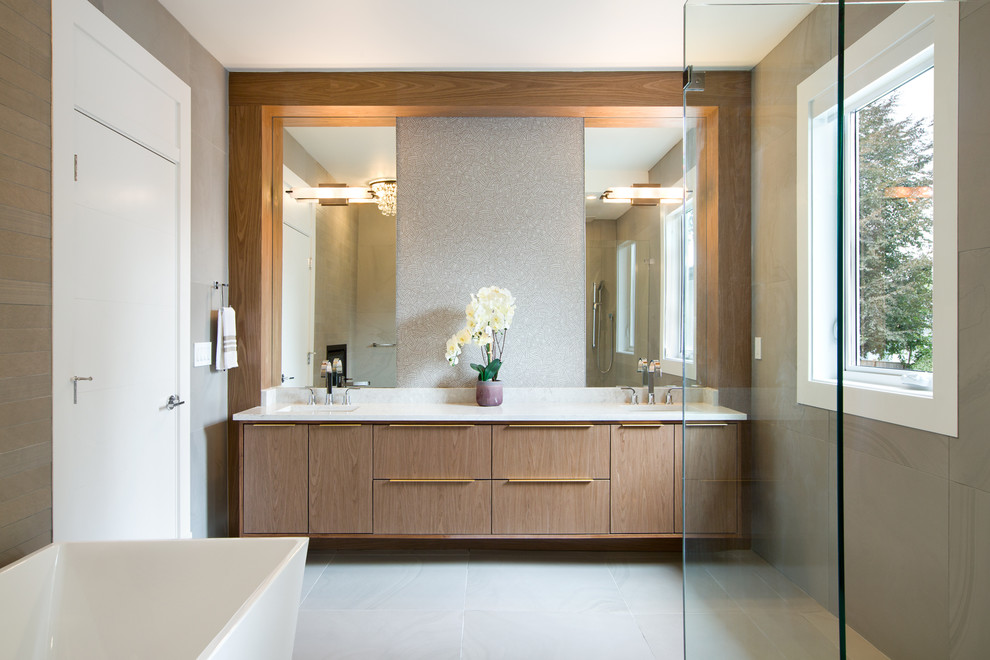 Photo of a medium sized modern ensuite bathroom in Vancouver with grey walls, grey floors, flat-panel cabinets, medium wood cabinets, a freestanding bath, a corner shower, grey tiles, ceramic tiles, a vessel sink, engineered stone worktops, a hinged door and white worktops.