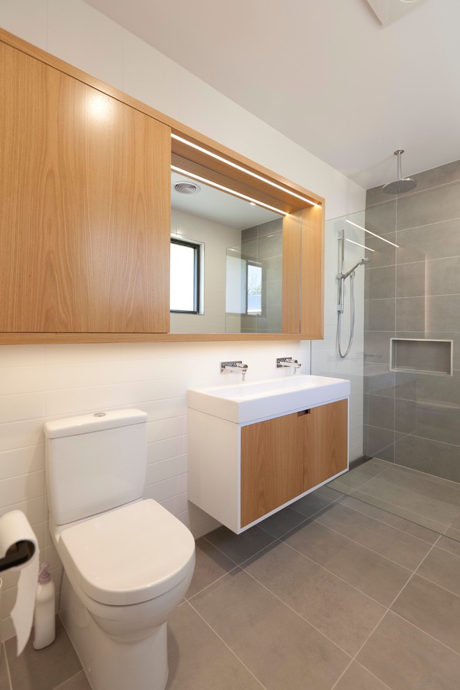 Modern inredning av ett stort en-suite badrum, med släta luckor, skåp i ljust trä, en öppen dusch, en toalettstol med separat cisternkåpa, grå kakel, cementkakel, vita väggar, cementgolv och ett väggmonterat handfat