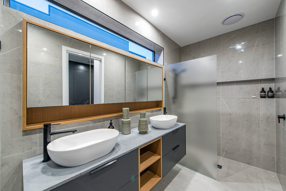 Cette image montre une salle de bain design avec un placard à porte plane, des portes de placard grises, une douche à l'italienne, un carrelage gris, un mur gris, une vasque, un sol gris, aucune cabine et un plan de toilette gris.