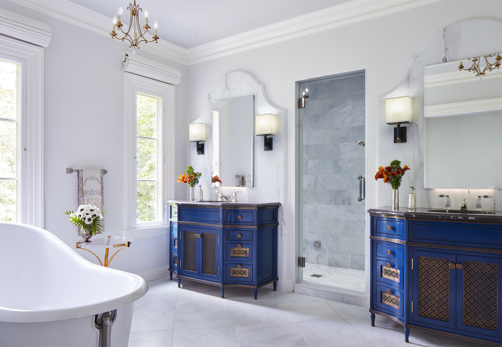 Cette image montre une salle de bain principale bohème avec un placard à porte shaker, des portes de placard bleues, une baignoire indépendante, un carrelage blanc, un mur gris, un lavabo posé, un sol gris et un plan de toilette noir.