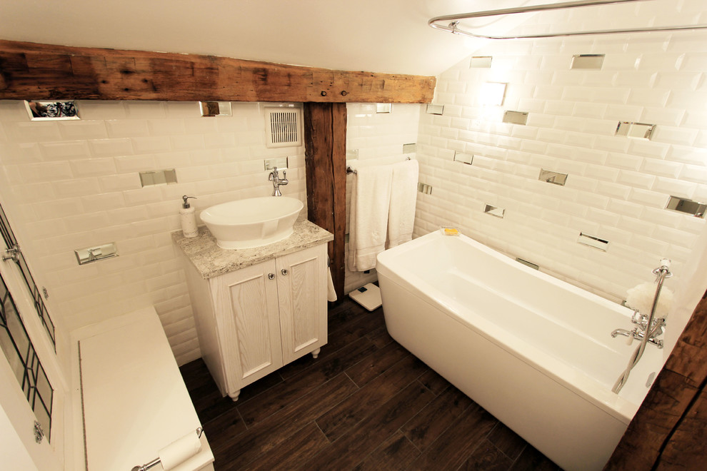 This is an example of a medium sized classic ensuite bathroom in Cleveland with raised-panel cabinets, white cabinets, a freestanding bath, a shower/bath combination, a one-piece toilet, white tiles, metro tiles, white walls, porcelain flooring, a vessel sink and engineered stone worktops.