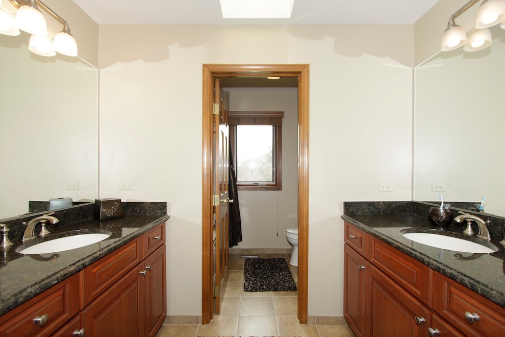 Bathroom - traditional beige tile and stone tile bathroom idea in Chicago with an undermount sink, raised-panel cabinets, medium tone wood cabinets, granite countertops and a two-piece toilet