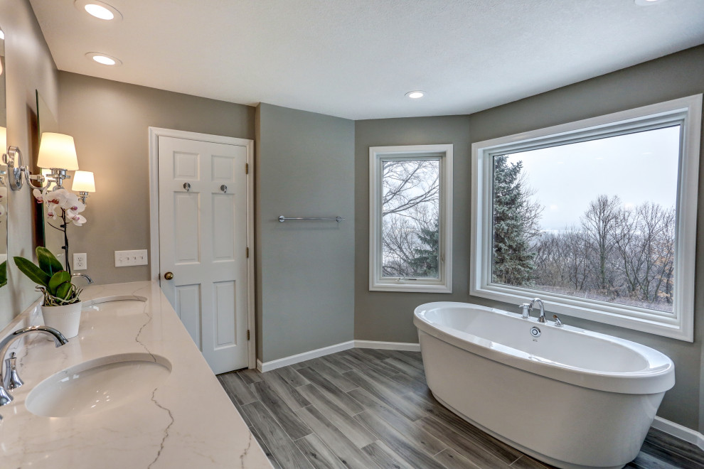 Photo of a large classic ensuite bathroom in Minneapolis with recessed-panel cabinets, grey cabinets, engineered stone worktops, grey worktops, a freestanding bath, an alcove shower, a two-piece toilet, grey tiles, metro tiles, grey walls, porcelain flooring, a submerged sink, grey floors and a hinged door.