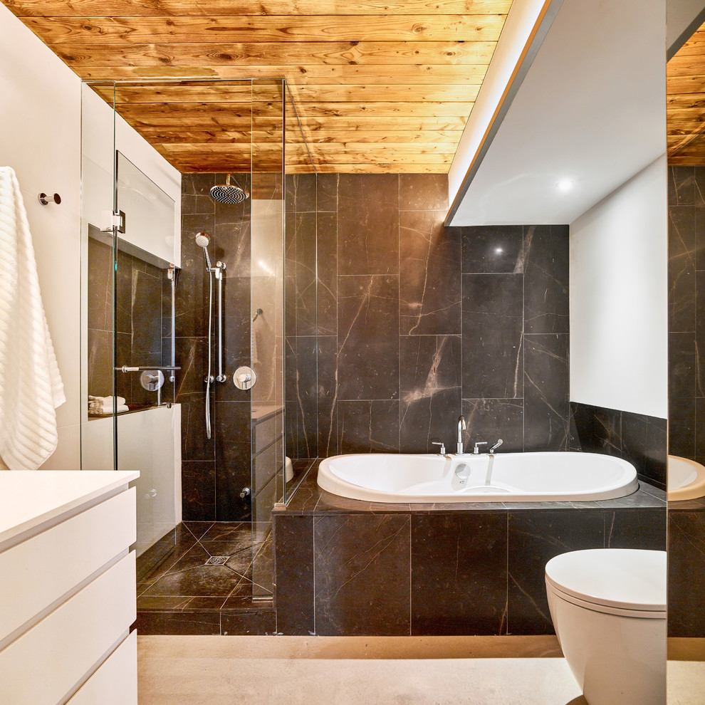 Пример оригинального дизайна: ванная комната в современном стиле с плоскими фасадами, белыми фасадами, накладной ванной, душем без бортиков, унитазом-моноблоком, черной плиткой, плиткой из известняка, белыми стенами, бетонным полом, врезной раковиной, столешницей из искусственного кварца, серым полом, душем с распашными дверями и белой столешницей