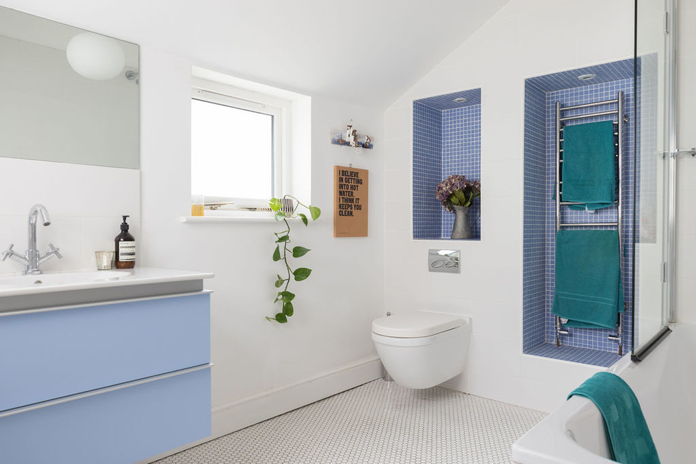 Cette image montre une salle de bain marine de taille moyenne pour enfant avec un placard à porte plane, des portes de placard bleues, une baignoire posée, un combiné douche/baignoire, WC suspendus, un carrelage bleu, mosaïque, un mur blanc, un sol en carrelage de terre cuite, un lavabo intégré, un plan de toilette en surface solide, un sol blanc, une cabine de douche à porte battante, un plan de toilette blanc, une niche, meuble simple vasque et meuble-lavabo suspendu.