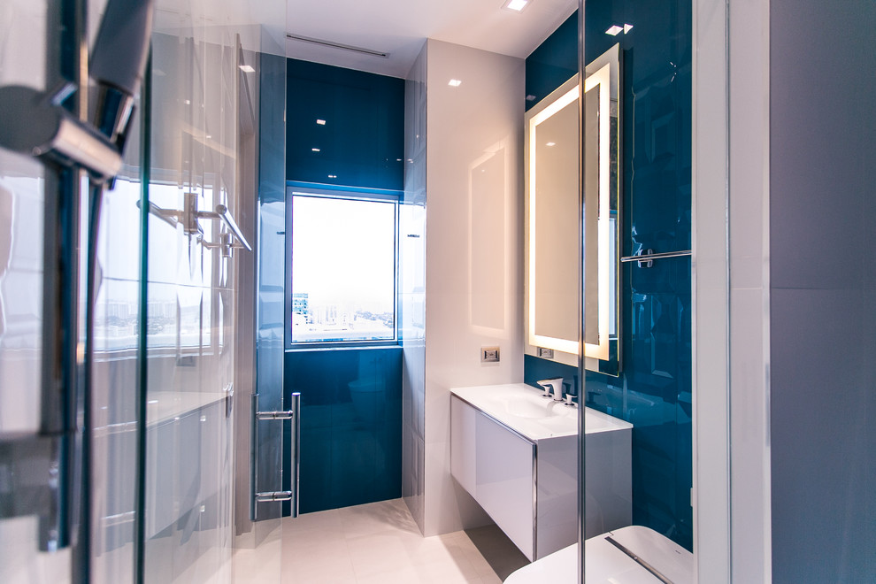 Exemple d'une douche en alcôve principale tendance de taille moyenne avec un placard à porte plane, des portes de placard blanches, WC à poser, un carrelage bleu, un carrelage blanc, un mur bleu, un sol en carrelage de porcelaine, un lavabo intégré, des carreaux de céramique et un plan de toilette en verre.