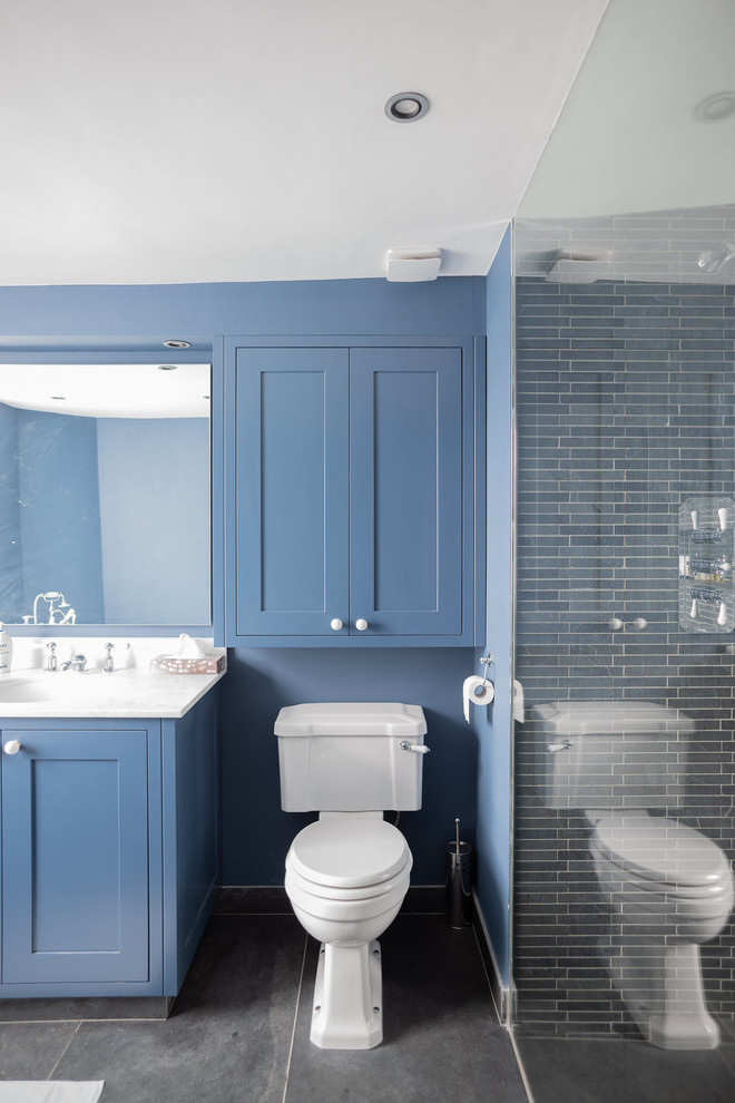 Design ideas for a large contemporary family bathroom in London with shaker cabinets, blue cabinets, a corner bath, a walk-in shower, a two-piece toilet, black tiles, slate tiles, blue walls, slate flooring, a submerged sink, marble worktops, grey floors, an open shower and white worktops.