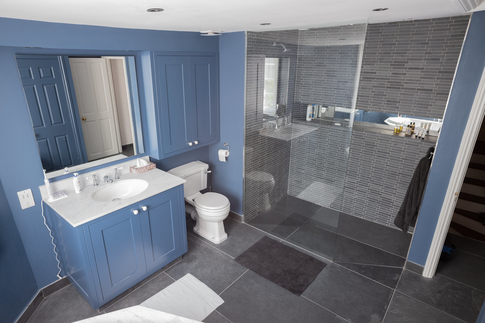 Design ideas for a large contemporary family bathroom in London with shaker cabinets, blue cabinets, a corner bath, a walk-in shower, a two-piece toilet, black tiles, slate tiles, blue walls, slate flooring, a submerged sink, marble worktops, grey floors, an open shower and white worktops.