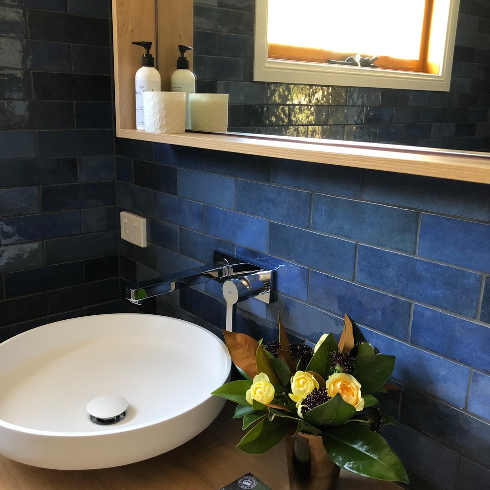 Exemple d'une salle de bain principale tendance en bois clair de taille moyenne avec un placard à porte plane, une douche ouverte, WC séparés, un carrelage bleu, des carreaux de céramique, un mur bleu, un sol en carrelage de céramique, une vasque, un plan de toilette en bois, un sol gris, aucune cabine et un plan de toilette beige.
