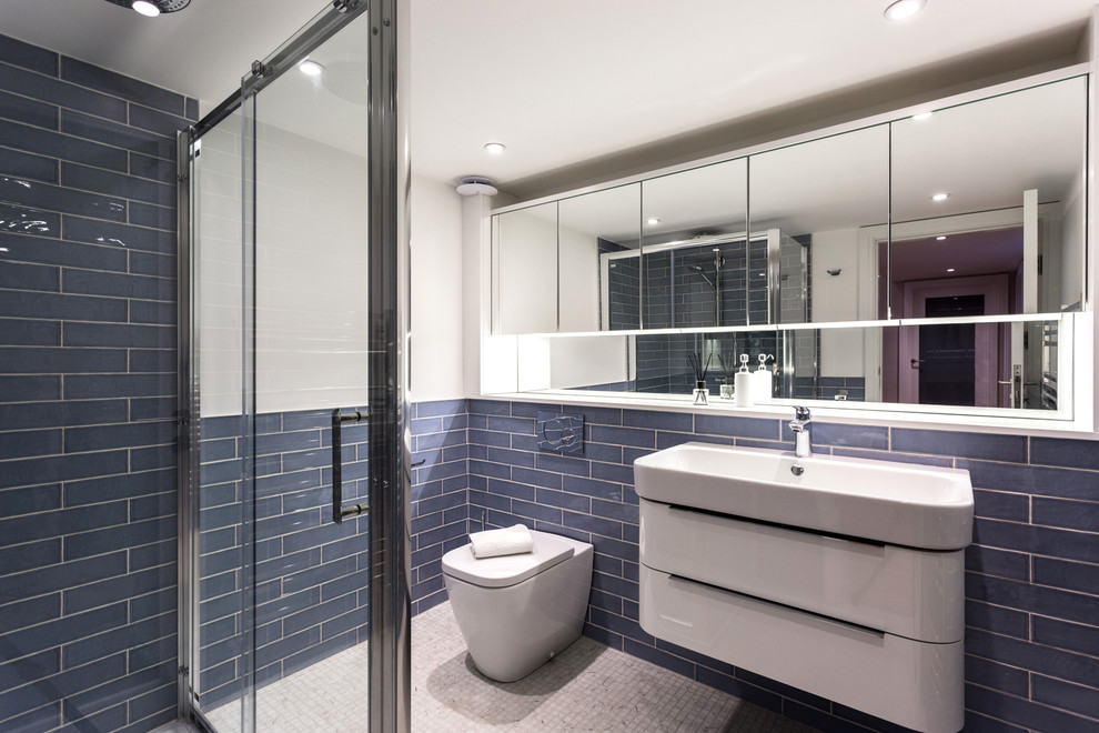 Foto på ett mellanstort funkis badrum med dusch, med en vägghängd toalettstol, blå kakel, keramikplattor, blå väggar, klinkergolv i keramik, ett avlångt handfat, vitt golv och dusch med skjutdörr
