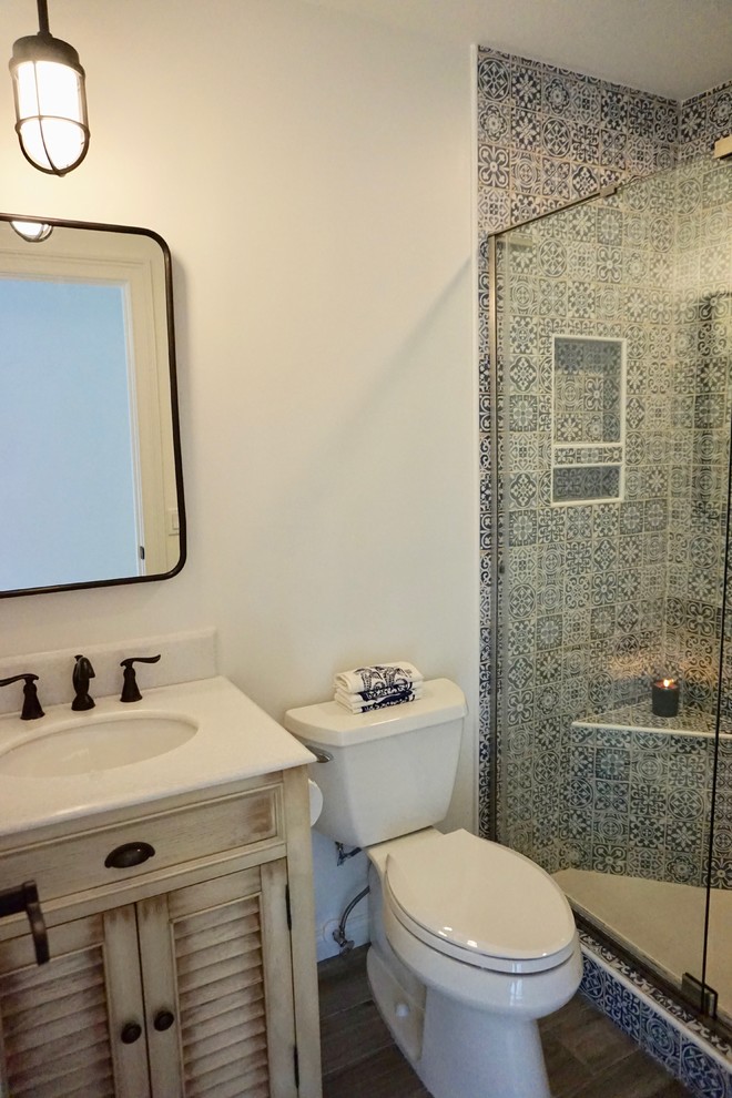 На фото: маленькая ванная комната в морском стиле с фасадами с филенкой типа жалюзи, бежевыми фасадами, душем в нише, раздельным унитазом, синей плиткой, керамической плиткой, белыми стенами, полом из керамогранита, душевой кабиной, врезной раковиной, столешницей из искусственного кварца, коричневым полом, душем с распашными дверями и белой столешницей для на участке и в саду с