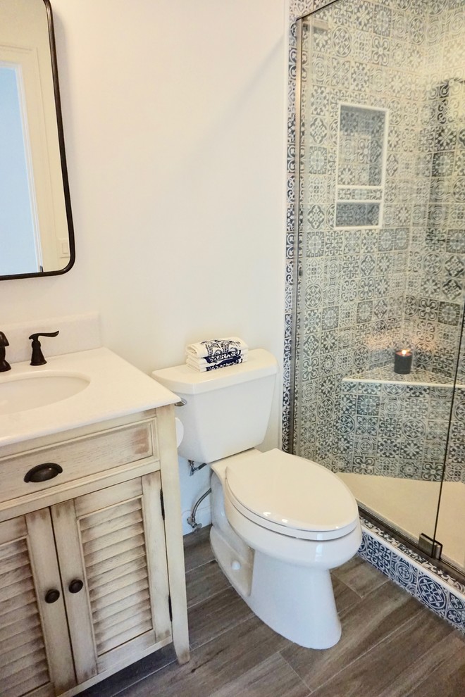 На фото: маленькая ванная комната в морском стиле с фасадами с филенкой типа жалюзи, бежевыми фасадами, душем в нише, раздельным унитазом, синей плиткой, керамической плиткой, белыми стенами, полом из керамогранита, душевой кабиной, врезной раковиной, столешницей из искусственного кварца, коричневым полом, душем с распашными дверями и белой столешницей для на участке и в саду с