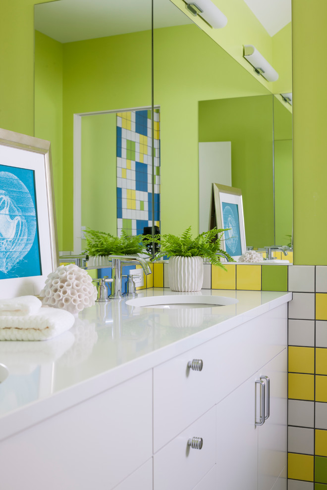 Inredning av ett modernt badrum, med ett undermonterad handfat, släta luckor, vita skåp, flerfärgad kakel och gröna väggar
