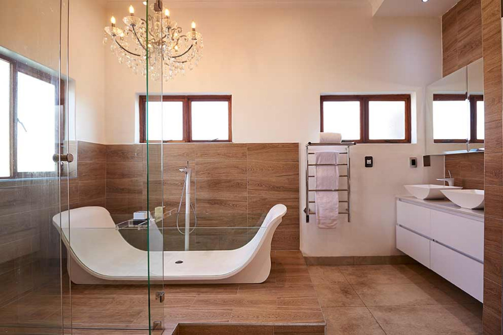 Идея дизайна: главная ванная комната среднего размера в средиземноморском стиле с белыми фасадами, отдельно стоящей ванной, двойным душем, инсталляцией, бежевой плиткой, плиткой под дерево, белыми стенами, полом из керамогранита, бежевым полом, душем с раздвижными дверями, белой столешницей, тумбой под две раковины и встроенной тумбой