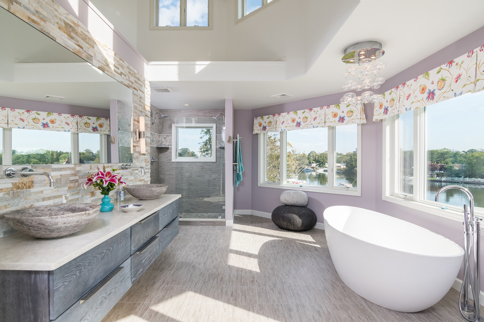This is an example of a medium sized traditional grey and purple ensuite bathroom in New York with flat-panel cabinets, a freestanding bath, grey tiles, stone tiles, purple walls, porcelain flooring, a vessel sink, granite worktops, grey cabinets, a double shower and grey floors.