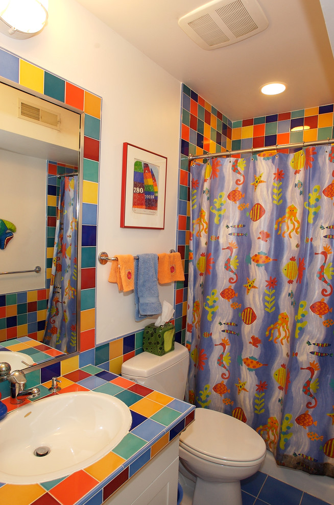 На фото: маленькая детская ванная комната в стиле фьюжн с накладной раковиной, фасадами в стиле шейкер, белыми фасадами, столешницей из плитки, ванной в нише, раздельным унитазом, разноцветной плиткой, керамической плиткой, белыми стенами, полом из керамической плитки и душем над ванной для на участке и в саду