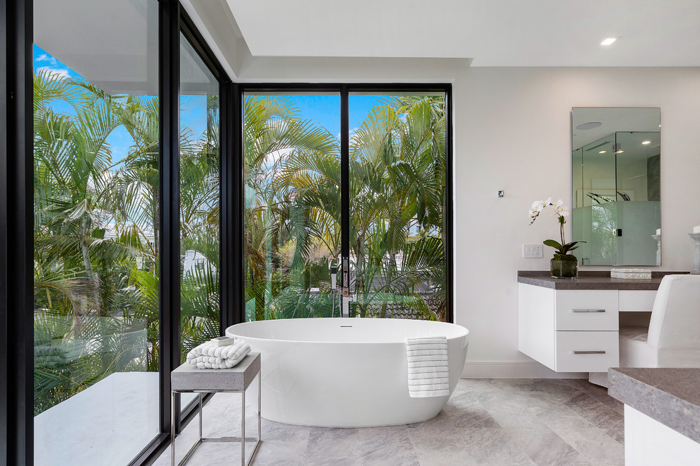 Modernes Badezimmer mit flächenbündigen Schrankfronten, weißen Schränken, freistehender Badewanne, grauer Wandfarbe, grauem Boden und brauner Waschtischplatte in Miami