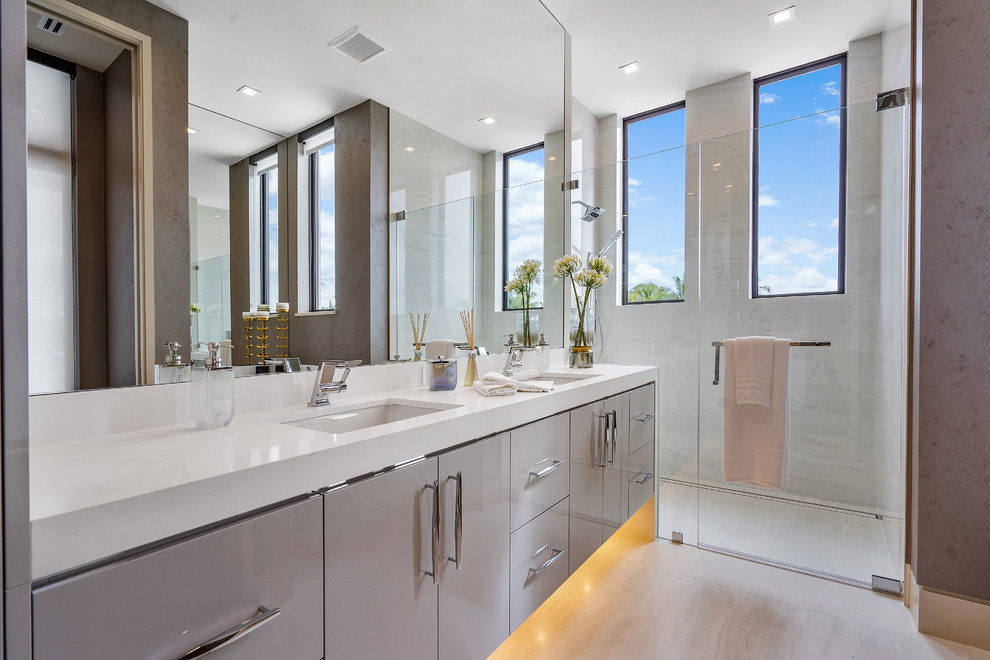 Großes Modernes Badezimmer En Suite mit flächenbündigen Schrankfronten, Steinplatten, Porzellan-Bodenfliesen, Unterbauwaschbecken, weißer Waschtischplatte, grauen Schränken, Duschnische, grauen Fliesen, grauem Boden und Falttür-Duschabtrennung in Miami