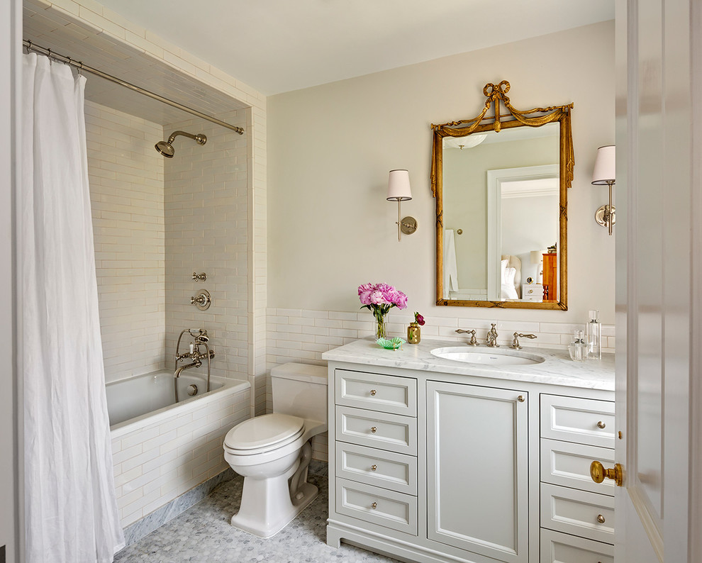 Klassisk inredning av ett badrum, med vita skåp, ett badkar i en alkov, en dusch/badkar-kombination, vit kakel, dusch med duschdraperi, tunnelbanekakel, beige väggar, mosaikgolv, ett undermonterad handfat och luckor med infälld panel