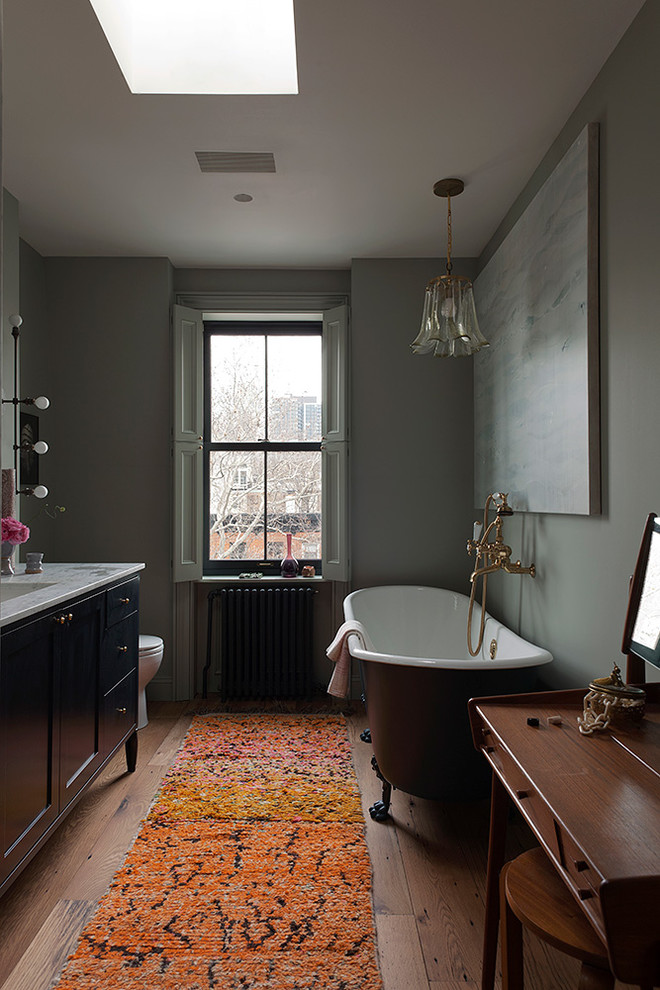 На фото: ванная комната в стиле неоклассика (современная классика) с синими фасадами, ванной на ножках, паркетным полом среднего тона и мраморной столешницей с