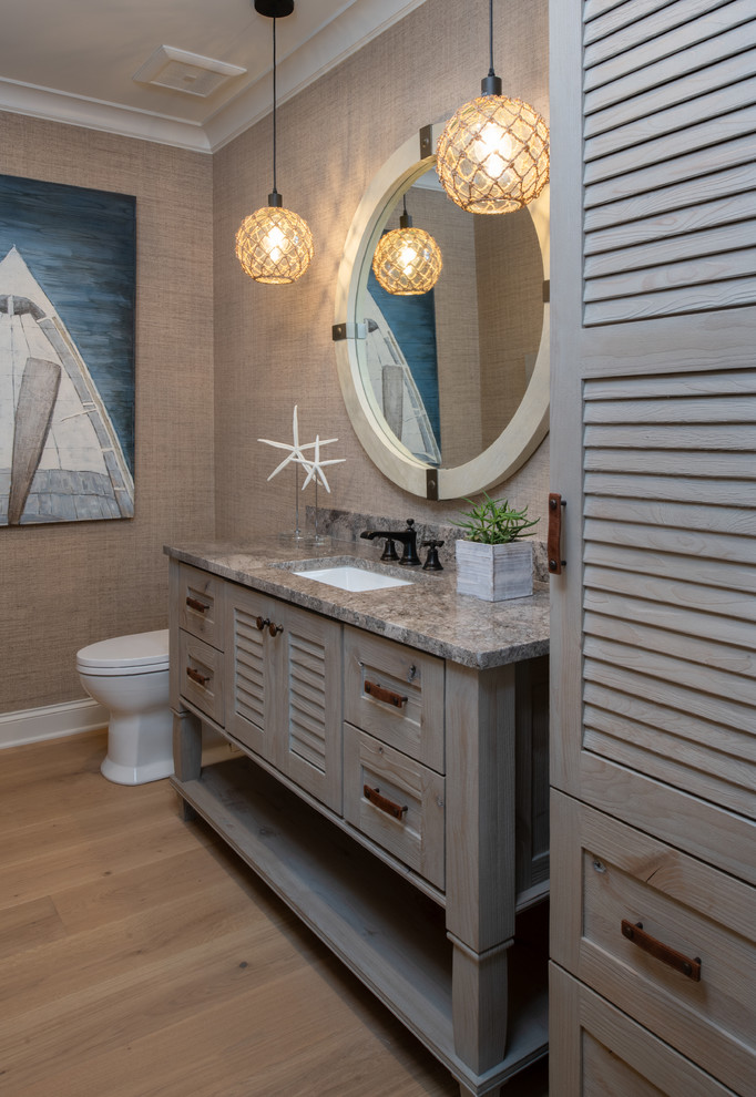 Modelo de cuarto de baño costero con armarios con puertas mallorquinas, paredes grises, suelo de madera clara, lavabo bajoencimera, encimeras grises y espejo con luz