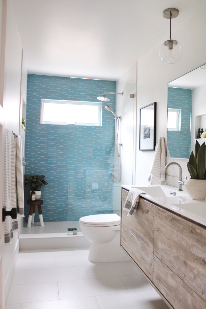 На фото: большая ванная комната в стиле модернизм с плоскими фасадами, светлыми деревянными фасадами, открытым душем, унитазом-моноблоком, зеленой плиткой, керамогранитной плиткой, белыми стенами, полом из керамогранита, душевой кабиной, монолитной раковиной, столешницей из искусственного камня, белым полом, открытым душем и белой столешницей с