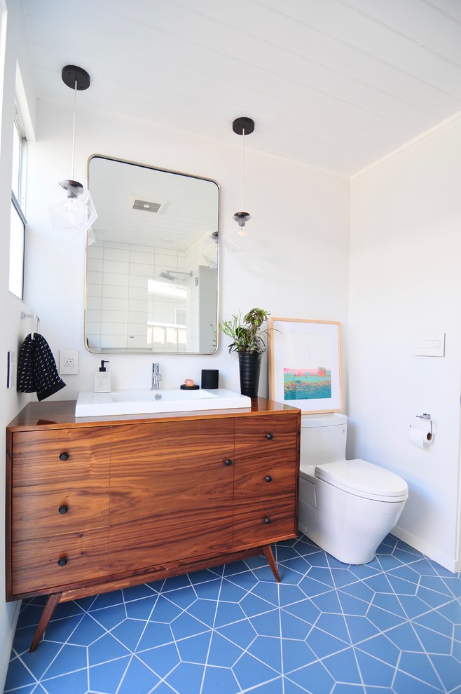Cette photo montre une salle de bain principale rétro en bois brun avec un carrelage blanc, des carreaux de céramique, un mur blanc, un sol en carrelage de céramique, un sol bleu, WC à poser, un lavabo posé, un plan de toilette en bois, un plan de toilette marron et un placard à porte plane.