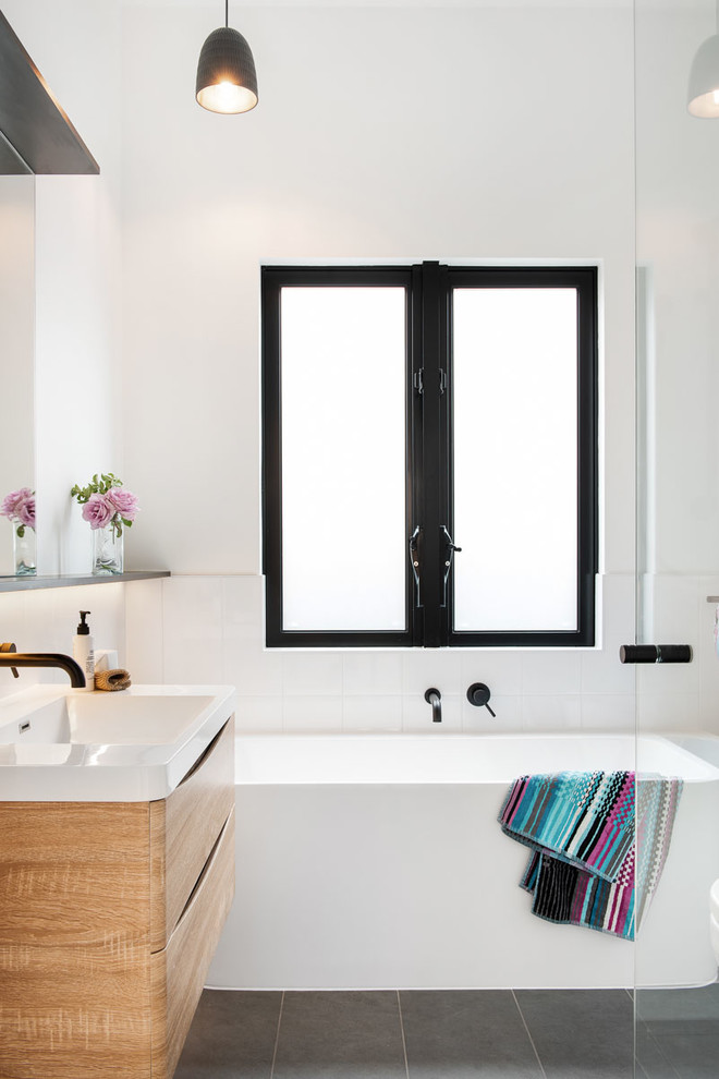 Exempel på ett modernt badrum, med skåp i ljust trä, ett fristående badkar, vit kakel, cementkakel, vita väggar, cementgolv, grått golv, släta luckor och ett konsol handfat