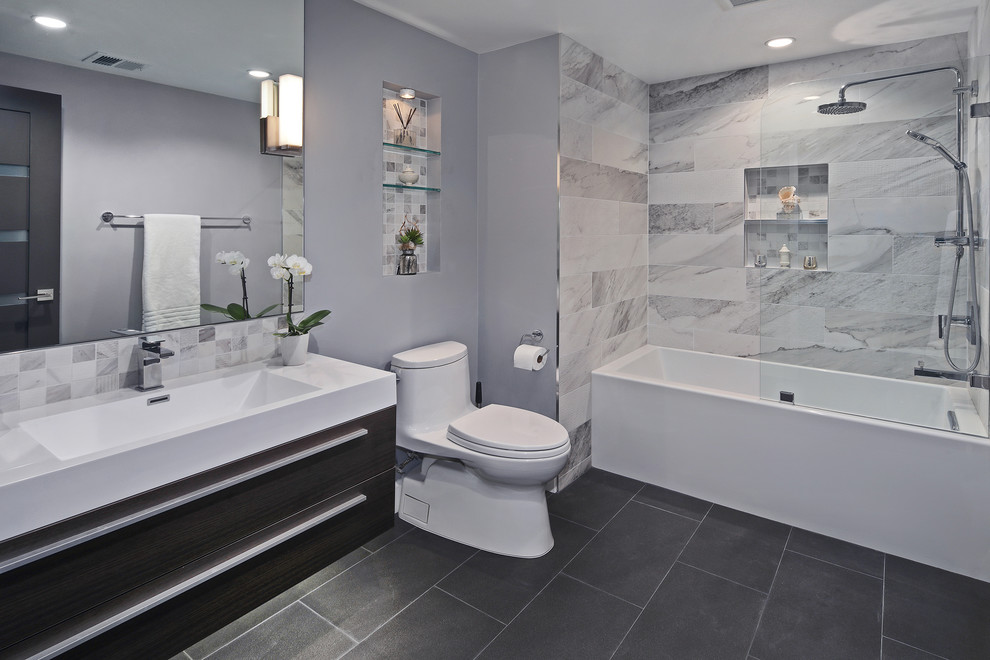Design ideas for a small contemporary bathroom in Orange County with flat-panel cabinets, dark wood cabinets, a shower/bath combination, grey tiles, porcelain tiles, grey walls, porcelain flooring, an integrated sink, an alcove bath, a two-piece toilet, black floors, a hinged door and engineered stone worktops.