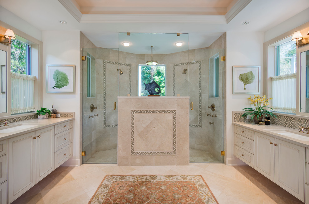 Inredning av ett klassiskt en-suite badrum, med ett undermonterad handfat, luckor med infälld panel, vita skåp, bänkskiva i kalksten, en dubbeldusch, beige kakel, porslinskakel, vita väggar och travertin golv