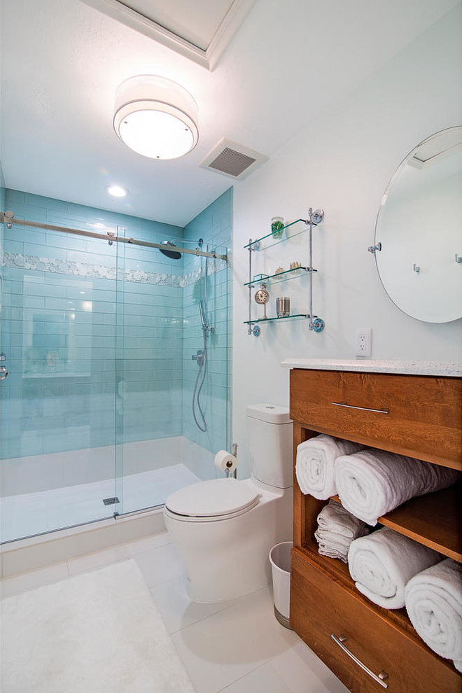 Bild på ett litet funkis en-suite badrum, med skåp i mellenmörkt trä, ett badkar i en alkov, en dusch i en alkov, glaskakel, klinkergolv i porslin, ett undermonterad handfat, bänkskiva i kvarts, en toalettstol med separat cisternkåpa, vita väggar, blå kakel och släta luckor