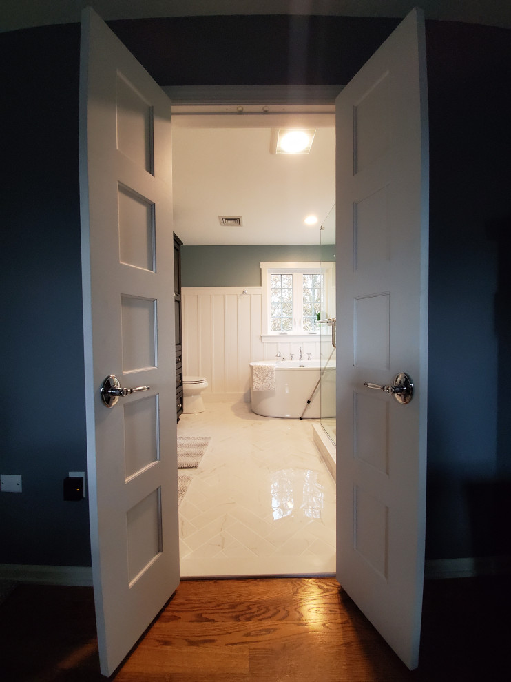 Aménagement d'une grande salle de bain principale craftsman en bois foncé avec un placard avec porte à panneau surélevé, une baignoire indépendante, une douche d'angle, WC séparés, un carrelage blanc, du carrelage en marbre, un mur bleu, un sol en carrelage de porcelaine, un lavabo encastré, un plan de toilette en quartz modifié, un sol blanc, une cabine de douche à porte battante et un plan de toilette blanc.