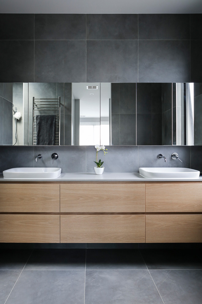 Пример оригинального дизайна: главная ванная комната среднего размера в современном стиле с светлыми деревянными фасадами, отдельно стоящей ванной, двойным душем, унитазом-моноблоком, серой плиткой, керамогранитной плиткой, серыми стенами, полом из керамогранита, накладной раковиной, столешницей из искусственного кварца, серым полом и открытым душем