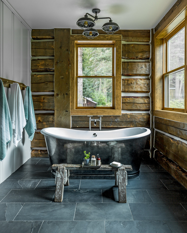 На фото: главная ванная комната в деревянном доме в стиле рустика с отдельно стоящей ванной, коричневыми стенами и серым полом