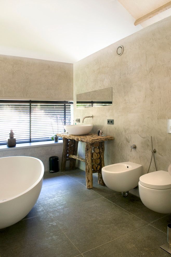 Immagine di una stanza da bagno minimal di medie dimensioni con vasca freestanding, pareti beige, lavabo a bacinella e WC sospeso