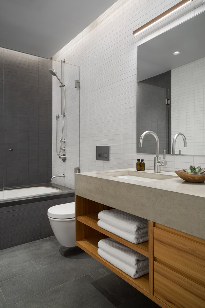 Foto på ett industriellt grå badrum, med öppna hyllor, ett undermonterat badkar, en dusch/badkar-kombination, grå kakel, vit kakel, ett undermonterad handfat, grått golv och skåp i ljust trä