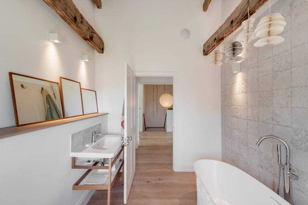 Medium sized contemporary ensuite bathroom in Devon with a freestanding bath, grey tiles, white walls, light hardwood flooring, a console sink and beige floors.