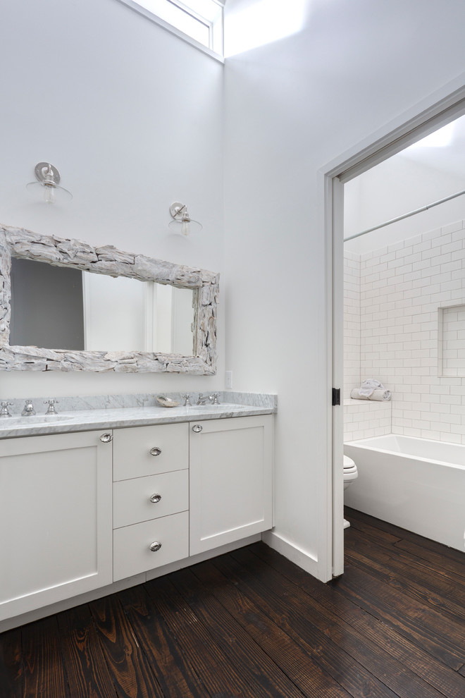 Photo of a large contemporary bathroom in Austin with a submerged sink, shaker cabinets, white cabinets, marble worktops, an alcove bath, a shower/bath combination, white tiles, ceramic tiles, white walls and dark hardwood flooring.