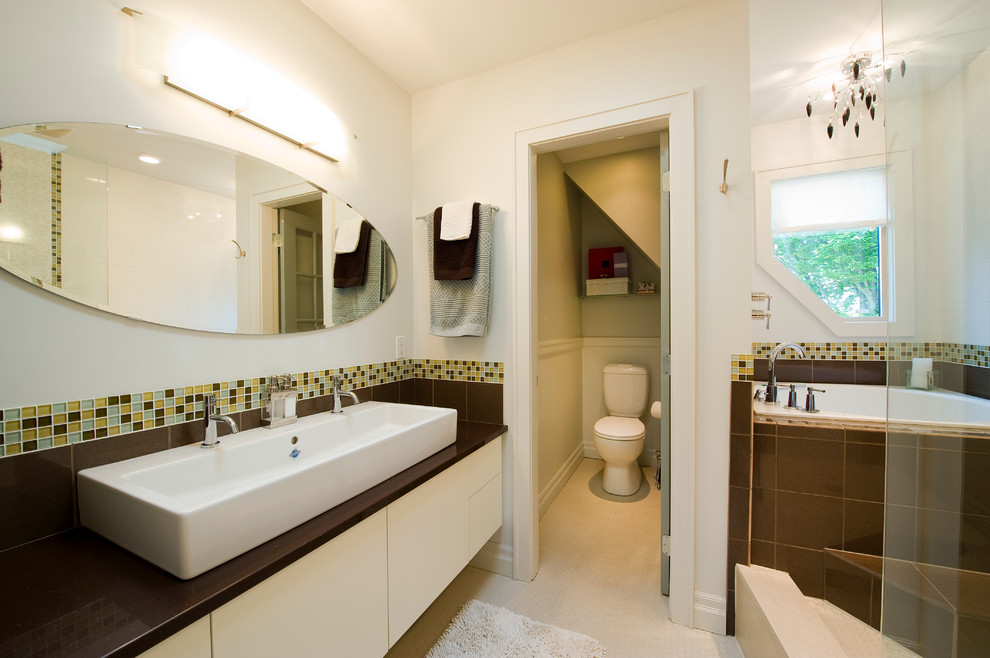 Modern inredning av ett en-suite badrum, med vita skåp, en dusch/badkar-kombination, ett fristående handfat, en toalettstol med separat cisternkåpa och ett badkar i en alkov